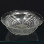 Bowl em meio cristal prensado, formato hemisférifco, borda ligeiramente revirada para fora, verso decorado  com caneluras verticais contínuas, interrompidas junto à borda por friso geométrico composto por elementos triangulares em relevo regular, com decoração radial em estrela lapidada, delimitada por anel liso, base anelar integrada ao molde. sem marca visível de fabricante. Med.: 8 x Diam.: 24,5 cm.