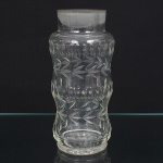 Garrafa(sem tampa) em cristal lapidado, translúcido e incolor, corpo cilíndrico com perfil levemente ondulado, apresentando boca circular de bordo polido e base circular espessa, decoração lapidada composta por faixas horizontais alternadas, com motivos geométricos e fitomórficos estilizados, incluindo folhas lanceoladas entrecruzadas, ovais facetados e gomos verticais. Parte inferior com estrela lapidada radial no fundo. Lapidação executada em baixo e médio relevo, com cortes regulares e repetitivos. Medidas: Alt.: 19,5 x Diam.: 8,5 cm.