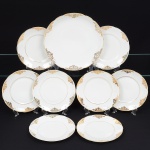 Porcelana Real, Mauá - SP(Fundada em 1943 por Fritz Erwin Schmidt). Conjunto pra sobremesa em porcelana nacional da década de 1950/60, esmaltagem vítrea na cor branca, dotada de geneosa decoração aplicada por douração, composta por motivos fitomórficos e arabescos simétricos distribuídos em reservas na aba, alternando elementos florais estilizados, folhagens e rendilhados geométricos, filetes acompanham o contorno da aba e o limite do centro. Composto de uma(01) travessa circular e oito(08) pratos para sobremesa. Marca da manufatura no verso. Medidas: Diam.: ; Diam.: