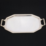 FRACALANZA. Belíssima bandeja confeccionada em metal espessurado à prata, formato octogonal, centro rebaixado, borda relevada com fileira de frisos e fitas cruzadas, padrão "Croisé", ornato replicado nas alças laterais, com terminações cinzeladas em folhagens. Marca da manufatura puncionada no verso. Medidas: Alt.: 3,5 x Comp.: 58(de uma alça a outra) x Larg.:  33 cm.