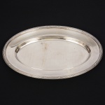 FRACALANZA. Elegante travessa oval confeccionada em metal espessurado à prata, centro ligeiramente rebaixado, borda relevada com fileira de frisos intercalados por fitas cruzadas, padrão "croisé". Marca da manufatura no verso. Medida: Comp. 41,5 x Larg.: 27 cm. Apresenta marcas de uso, visíveis nas fotos.