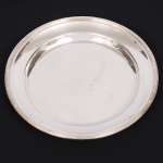 FRACALANZA. Elegante travessa circular confeccionada em metal espessurado à prata, centro ligeiramente rebaixado, borda relevada com fileira de frisos intercalados por fitas cruzadas, padrão "croisé". Marca da manufatura no verso. Medida: Diam.: 30,5 cm.