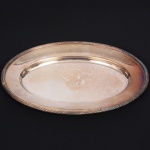 FRACALANZA. Elegante travessa oval confeccionada em metal espessurado à prata, centro ligeiramente rebaixado, borda relevada com fileira de frisos intercalados por fitas cruzadas, padrão "croisé". Marca da manufatura no verso. Medida: Comp. 36 x Larg.: 24 cm. Apresenta marcas de uso, visíveis nas fotos. Necessita apenas de polimento.