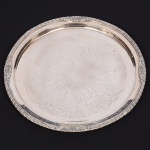 BELPRATA. Bandeja circular confeccionada em metal espessurado à prata, centro ligeiramente rebaixado, lavrado com composição de motivo fitomórfico, borda relevada com frisos e elementos florais. Marca da manufaura no verso. Med.: Diam. 31,5 cm.