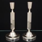 BRISTOL PRATA 90. Elegante par de castiçal confeccionado em metal espessurado à prata, fuste maciço de seção quadrangular, bobeche obcônica, base cicular de centro elevado. Marca da manufatura ao fundo. Med.: Alt.: 23 x Diam.: 10 cm.