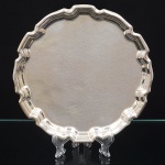 Bandeja porta-cartão(card tray) confeccionada em metal espessurado à prata, executada ao estilo inglês do período georgiano, formato circular, centro ligeiramente rebaixado, borda repuxada e recortada. Medida: Diam.: 21 cm.