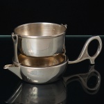 EBERLE(Abramo, Eberle & Co.) Elegante coador de chá confeccionado em metal espessurado à prata, acompanha seu respectivo dosador. Marca da manufatura puncionada na alça. Med.: Alt. 5 x Comp. 12,5 x Larg. 6 cm.