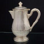 BELPRATA. Belíssima cholateira em metal espessurado à prata, executado ao estilo inglês do período Vitoriano. Bojo em forma de balaústre repuxado com godrões relevados, que se replicam na tampa, dotada de abertura através de movimento basculante, encimada por puxador em feitio de fruto, assente sobre base circular moldada em degraus, bico vertedor traingular revirado para fora, alça lateral em voluta com terminações cobertas por folhagens. Marca da manufatura no verso. Med.: Alt. 21,5 x Comp. 18 x Larg. 11 cm.