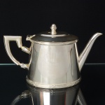 FRACALANZA. Elegante bule para chá confeccionado em metal espessurado à prata, corpo cônico decorado nas bordas com fileira de frisos e fitas cruzadas, padrão "croisé", obtido através da técnica do cinzelado, alça lateral curvada de topo retilíneo, bico vertedor tubular de ponta ligeiramente curvada, tampa dotada de abertura através de movimento basculante, encimada por puxador ovoide. Marca da manufatura puncionada ao fundo. Med.: Alt. 13 x Comp. 21,5 x Larg. 10 cm.