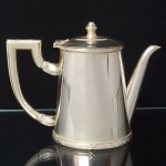 FRACALANZA. Elegante bule para café confeccionado em metal espessurado à prata, corpo cônico decorado nas bordas com fileira de frisos e fitas cruzadas, padrão "croisé", obtido através da técnica do cinzelado, alça lateral curvada de topo retilíneo, bico vertedor tubular de ponta ligeiramente curvada, tampa dotada de abertura através de movimento basculante, encimada por puxador ovoide. Marca da manufatura puncionada ao fundo. Med.: Alt. 16 x Comp. 20,5 x Larg. 9 cm.