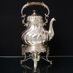 Excepcional samovar confeccionado em metal espessurado à prata, bule com bojo em balaústre, repuxado com fileira de gomos espiralados, replicados na tampa, bico vertedor curvilíneo de ponta revirada, alça articulável com pega em madeira, base dotada de pinos de segurança que permitem inclinação para ambos os lados, assentado sobre trés pernas curvas em forma de folhagem, encimadas por medalhões, apresenta queimados original. Pega da tampa em madeira adaptada. Medidas: Alt.: 40 x Comp.: 23 x Larg.: 19 cm.