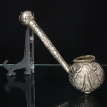 Antiga guampa confeccionada em metal espessurado à prata, composto por reservatório globular em forma de coco, decorado em relevo com folhas estilizadas e áreas pontilhadas, borda com aro moldado em cordame. Cabo longo tubular, segmentado, decorado com elementos geométricos e florais em relevo, terminando em pomo esférico. Execução por técnicas de repuxo, cinzelagem e soldagem. Medida: Comp.: 27 cm. Apresenta amolgadela no cabo.