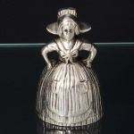 Antiga sineta de mesa confeccionada em metal em espessurado à prata, executada na forma de camponesa com vestes de estilo vitoriano. Marca da manufatura ao fundo. Med.: Alt. 7,5 x Diam.: 5 cm.