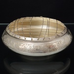 Floreira executada em metal espessurado à prata, decoração relevada com motivos florais e folhagens ao redor do corpo, formato circular, achatado e alargado, borda superior dotada de grade metálica cruzada, para arranjos florais. Med.: Alt. 6 x Diam. 14 cm.