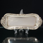 Antiga bandeja para espevitadeira confeccionada em metal espessurado à prata, formato oblongo de extremos arredondados, borda relevada com flores e folhagens, assentado sobre quatro pés semiesféricos. Medidas: Alt.: 2,5 x Comp.: 26 x Larg.: 10 cm.