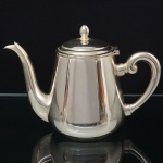 WOLFF. Elegante bule para chá confeccionado em metal espessurado à prata, bojo liso de formato aproximadamente cônico, tampa ligeiramente abaulada, encimada por puxador ovoide, dotada de abertura através de movimento basculante, bico vertedor curvilíneo de ponta recortada, alça lateral em voluta. Marca da manufatura puncionada ao fundo. Medidas: Alt.: 13 x Comp.: 20 x Larg.: 10 cm.
