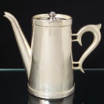 MAGNA PRATA 90. Bule para café confeccionado em metal espessurado à prata, bojo obcônico com bodas superior e inferior relevadas, tampa circular com puxador torneado, bico vertdor tubular de ponta curvada e recortada, alça lateral em voluta. Marca da manufatura ao fundo. Medidas: Alt.: 15 x Comp.: 18,5 x Larg.: 9 cm.