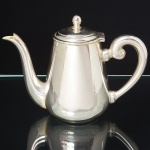 WOLFF. Elegante bule para café confeccionado em metal espessurado à prata, bojo liso de formato aproximadamente cônico, tampa ligeiramente abaulada, encimada por puxador ovoide, dotada de abertura através de movimento basculante, bico vertedor curvilíneo de ponta recortada, alça lateral em voluta. Marca da manufatura puncionada ao fundo. Medidas: Alt.: 14 x Comp.: 19 x Larg.: 9 cm.