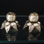 Par de castiçais confeccionados em metal espessurado à prata, executados em forma de flor, base sobre folhagens reviradas para baixo. Medidas: Alt.: 7 x Diam.: 8 cm.
