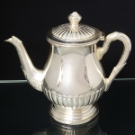 BELPRATA. Belíssimo bule para café em metal espessurado à prata, executado ao estilo inglês do período Vitoriano. Bojo em forma de balaústre repuxado com godrões relevados, que se replicam na tampa, dotada de abertura através de movimento basculante, encimada por puxador em feitio de fruto, assente sobre base circular moldada em degraus, bico vertedor curvilíneo de ponta recortada, coberto por folhas de acanto, alça lateral em voluta com terminações cobertas por folhagens. Marca da manufatura no verso. Med.: Alt. 21,5 x Comp. 20 x Larg. 11 cm.