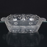 Travessa executada em vidro prensado, diáfano e incolor, formato retangular, ricamente gravado com flores e elementos vegetalistas, centro rebaixado, dotado de duas divisões, borda ondulada e recortada, alças laterais conchiforme integradas a borda. Medidas: Alt.: 4,5 x Comp.: 19,5 x Larg.: 15,5 cm.