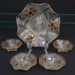 Conjunto em vidro moldado, acabamento acetinado, dotado de rica decoração de flores iridescentes e elementos geométrico em baixo relevo, borda ondulada e contornada por friso em douradura(apresenta desgaste, assente sobre três pés integrados. Composto de uma(01) saladeira e quatro(04) taças. Medidas: Alt.: 9 x Diam.: 28 cm; Alt.: 5 x Diam.: 14 cm. Todos apresentam bicado nos pés.