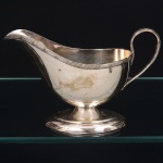 Molheira confeccionada em metal espessurado à prata, fabricação estadunidense, formato navicular de interior côncavo, base oblonga elevada, alça lateral curvada, borda ondulada com vertedouro revirado para fora. Marca da manufatura ao fundo. Medidas: Alt.: 11,5 x Comp.: 19 x Larg.: 9 cm. Necessita polimento.