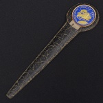 Abridor de correspondência comemorativo, lâmina metálica plana e afilada, com seção reta e extremidade pontiaguda. Empunhadura circular esmaltada, decorada com emblema do Programa Apollo XIII, com representação figurativa e inscrições. Haste com inscrição gravada Kennedy Space Center  Florida. Acompanha estojo em couro, formato alongado, com costuras aparentes. Objeto relacionado ao programa espacial norte-americano. Medida: Comp.: 18 cm.