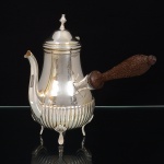 REBOUÇAS PRATA 90. Bule confeccionada em metal espessurado à prata, estilo inglês; bojo piriforme decorado com sucessão de gomos verticais na parte inferior, obtidos através da técnica do repuxado, bico vertedor curvilíneo de ponta recortada, tampa campaniforme encimada por puxador em pináculo, dotada de abertura através de movimento basculante, assentado sobre três pés de espátula curvada sob concha, alça lateral executada em madeira torneada. Marca da manufatura ao fundo. Medidas: Alt.: 18,5 x Comp.: 20 x Larg.: 12 cm. Apresenta desgaste no banho de prata localizado ao redor da borda.