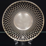 AUREA PRATA 90. Fruteira confeccionada em metal espessurado à prata, formato circular, centro liso, orla vazada com trama geométrica regular em padrão entrecruzado. Marca da manufatura no verso. Medida: Diam.: