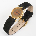 CARTIER, Paris - França(Fundada em 1847 por Louis-François Cartier). Relógio de pulso feminino, série Must de Cartier, modelo Vendôme (Ronde Vendôme). Caixa circular confeccionada em prata 925 com plaqué or 20 microns. Mostrador analógico com composição concêntrica, ponteiros centrais, assinatura Cartier e indicação Swiss. Coroa lateral com cabochão azul. Movimento a quartzo. Verso da caixa com inscrições gravadas: Cartier Paris, Quartz, Argent, Plaque Or G 20M, numeração e códigos de referência. Pulseira em couro siténtico(trocada). Não está funcionando. Acondicionado em caixa original(apresenta marcas do tempo e de uso. Medida da caixa: Diam.: 27 mm.