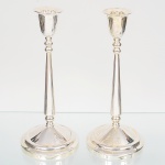 Par de castiçais em metal espessurado à prata, bocal obcônico, coluna longa afilada, intercalada por nós ovóides dispostos em sequência vertical, e base circular escalonada. Acondicionado em caixa original. Medidas: