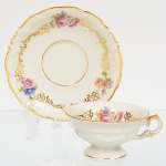 KPM - Krister Porzellan-Manufaktur, Waldenburg - Alemanha(Fundada em 1831 por Karl Kristen). Excepcional chávena para café em porcelana de manufatura alemã, fabricada na polônia entre anos de 1930-1945, modelo Friederike, citado na Enciclopédia de Porcelana da Silésia Volume I. Série "Royal Ivory". Executado ao estilo renascentista. Esmaltagem vítrea de tom marfim, modelada com elementos fitomorfos em relevo, decorada com flores soltas em estampagem policromada, e generosos arremates de frisos em douraudura, chávena de bojo campaniforme, assente sobre base alta de formato circular e alça lateral em voluta, padrão decorativo replicado no pires.Marca da manufatura no verso. Meds.: Chávena: Alt. 4 x Comp. 9,5 x Larg. 8 cm. Pires: Diam. 12 cm.