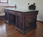 Grande escrivaninha do começo do século XX estilo império em madeira nobre almofadada, quatro colunas espirais, nove gavetas. Acompanha cadeira de braços e giratória do mesmo período.