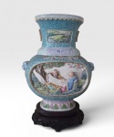 Vaso em porcelana chinêsa policromado, ricamente trabalhado com alto relevo, cenas de paisagem a beira de um lago, dois personagems em um barco. Possui alças laterais em formato de cabeças. Assinado na base e repousa sobre uma base em madeira esculpida. China, inicio do século XX.