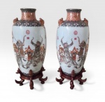 Par de vasos em porcelana chinesa, ricamente trabalhados em tons de vermelho e dourado simbolizando a prosperidade. Segundo a tradição chinesa, o vermelho é símbolo de felicidade, sucesso, beleza, vitalidade e boa sorte. Os vasos possuem decoração em torno deles com cenas de personagens portando simbolos de prosperidade e boa fortuna. O pescoço dos vasos é trabalhado com flores estilisadas e com o Lu, um símbolo chinês muito popular , que significa prosperidade. Os vasos possuem alças em forma de morcego, que na cultura chinesa é o símbolo da graça, ventura e felicidade. Assinados na base e repousam sobre uma base ricamente esculpida em madeira. China, início do século XX.