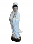 Figura em porcelana representando Guan Yin a deusa da Misericórdia. A figura é primorosamente estilizada, com um coque alto e vestida com um longo manto branco esmaltado com bordas vermelhas permitindo que seus dedos dos pés apareçam. A figura de Guanyin exala serenidade com um sorriso agradável e pacífico, complementado por pálpebras ligeiramente semicerradas e ela porta um colar de jade símbolo da realeza. Suas cinco principais virtudes são a misericórdia, modéstia, coragem, justiça e sabedoria. Ela é vista como uma alma que alcançou a iluminação plena e não precisa mais reencarnar,  no entanto, escolhe fazê-lo para iluminar os outros. A porcelana repousa sobre uma base em madeira entalhada. Em boa condição, somente possui um fio de cabelo nas costas.