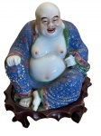 Figura em porcelana policromada representando um Buda Risonho, também chamado Budai ou Buda Chinês. Figura importante na tradição popular asiática, particularmente no budismo, taoísmo e xintoísmo, seu nome significa saco de pano, que vem do saco que carregava, cheio de comida e presentes para os pobres. Ele representa generosidade, fortuna e abundância. Nesta representação ele segura em uma mão um komboloi, que é um objeto originário da China que se assemelha a um pequeno rosário e que são usados em várias religiões para registrar orações e acalmar a mente. Possui assinatura em sua base. China, inicio do século XX.