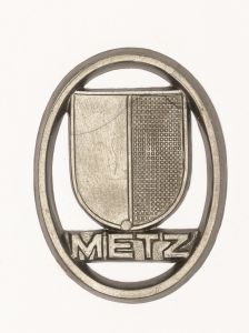 Militaria, Alemanha II Guerra. Proveniente de importante coleção adquirida em Ciney - Bélgica (Feira gigantesca de Militaria). O partido nazista promoveu uma grande arrecadação de fundos antes e durante a guerra com a venda de grande variedade de itens colecionáveis, pins, pendentes, tinnies, badges etc. Todos colecionáveis para incentivar novas compras. Como referência para estudo e identificação aconselhamos o catálogo Donation Badges, Pins & Pendants of the Third Reich de Joseph Cassidy & Christopher Alexander. Oportunidade para colecionador avançado. *Item não promove ou glorifica violência ou intolerância racial. Está à venda apenas para fins de preservação da memória histórica. A Organização do leilão não faz apologia a quaisquer movimentos políticos ou ideológicos, e repudia qualquer ideologia de cunho racista.  1941. Brasão de cidade ocupada ou fronteira alemã. 38x29 mm. Pág. 237 a 238. Metz.