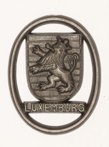 Militaria, Alemanha II Guerra. Proveniente de importante coleção adquirida em Ciney - Bélgica (Feira gigantesca de Militaria). O partido nazista promoveu uma grande arrecadação de fundos antes e durante a guerra com a venda de grande variedade de itens colecionáveis, pins, pendentes, tinnies, badges etc. Todos colecionáveis para incentivar novas compras. Como referência para estudo e identificação aconselhamos o catálogo Donation Badges, Pins & Pendants of the Third Reich de Joseph Cassidy & Christopher Alexander. Oportunidade para colecionador avançado. *Item não promove ou glorifica violência ou intolerância racial. Está à venda apenas para fins de preservação da memória histórica. A Organização do leilão não faz apologia a quaisquer movimentos políticos ou ideológicos, e repudia qualquer ideologia de cunho racista.  1941. Brasão de cidade ocupada ou fronteira alemã. 38x29 mm. Pág. 237 a 238. Luxemburgo.