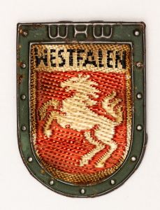 Militaria, Alemanha II Guerra. Proveniente de importante coleção adquirida na Bélgica - Feira de Militaria de Ciney. O partido nazista promoveu uma grande campanha de arrecadação de fundos antes e durante a guerra, com a venda de itens colecionáveis, pins, pendentes, tinnies, badges etc. Sempre colecionáveis voltada a novas compras. Oportunidade para colecionador avançado. **Item não promove ou glorifica violência ou intolerância racial. Está à venda apenas para fins de preservação da memória histórica. A Organização do leilão não faz apologia a quaisquer movimentos políticos ou ideológicos, e repudia qualquer ideologia de cunho racista. Campanha de Inverno WHW em tecido e metal. Westfalen. 31x43 mm.