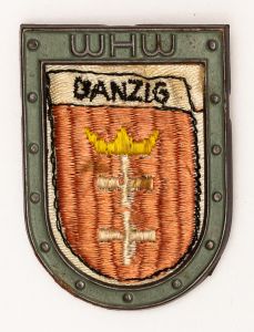 Militaria, Alemanha II Guerra. Proveniente de importante coleção adquirida na Bélgica - Feira de Militaria de Ciney. O partido nazista promoveu uma grande campanha de arrecadação de fundos antes e durante a guerra, com a venda de itens colecionáveis, pins, pendentes, tinnies, badges etc. Sempre colecionáveis voltada a novas compras. Oportunidade para colecionador avançado. **Item não promove ou glorifica violência ou intolerância racial. Está à venda apenas para fins de preservação da memória histórica. A Organização do leilão não faz apologia a quaisquer movimentos políticos ou ideológicos, e repudia qualquer ideologia de cunho racista.. Campanha de Inverno WHW em tecido e metal. 31x43 mm. Danzig. Peça repleta de história!.