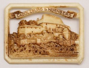 Militaria, Alemanha II Guerra. Proveniente de importante coleção adquirida na Bélgica - Feira de Militaria de Ciney. O partido nazista promoveu uma grande campanha de arrecadação de fundos antes e durante a guerra, com a venda de itens colecionáveis, pins, pendentes, tinnies, badges etc. Sempre colecionáveis voltada a novas compras. Oportunidade para colecionador avançado. **Item não promove ou glorifica violência ou intolerância racial. Está à venda apenas para fins de preservação da memória histórica. A Organização do leilão não faz apologia a quaisquer movimentos políticos ou ideológicos, e repudia qualquer ideologia de cunho racista. Castelo de Cadolzburg. Nuremberg. 43x33 mm.