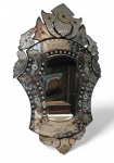Elegante espelho veneziano de parede, com moldura inteiramente composta por placas de cristal bisotado e lapidado à mão. A peça apresenta rica decoração floral gravada nas superfícies espelhadas, além de apliques em relevo que compõem a ornamentação superior e inferior, com destaque para o medalhão central em forma de escudo e arabescos laterais.  . Medindo 90 x  56 x 2 cm  Marcas do tempo , veja imagens extras.