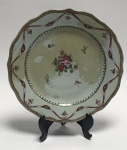 China, Cia das Índias, Dinastia Qing. Reinado Qianlong (1736-1795).  Excelente porcelana Jingdezhen de pasta dura, Famille Rose, pintura overglazed.  Prato de porcelana de pasta dura, recortado na borda. Cores rosa, rouge de fer, verde, aubergine e dourado.  Arranjo floral ao centro, fitas coloridas com dourado. No verso há marcas de pinos (suportes) de queima, garantia de uma queima perfeita. Há película na frente do prato, mas sem nenhuma marca de restauro no verso, antigo em bom estado.Diâmetro 23 cm.
