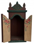 Oratório de mesa em madeira policromada, com portas duplas pintadas à mão em motivos florais, frontão recortado e detalhes entalhados. Peça de caráter devocional e decorativo, típica da arte popular brasileira. Apresenta pátina original e sinais de uso compatíveis com a idade. Mede 45 x 21 cm.