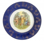 ENGLAND - Prato de coleção em porcelana cinglesa om ampla aba azul cobalto ricamente ornamentada com douração floral. Medalhão central policromado com cena alegórica clássica, representando figuras femininas em ambiente campestre, de inspiração mitológica. Marca no verso indicando procedência europeia, produção do século XIX. Peça de apelo decorativo e colecionável. Mede 25,5 cm.