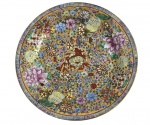 Prato em porcelana oriental ricamente esmaltado, com decoração floral policromada sobre fundo dourado, apresentando flores, frutos e elementos ornamentais finamente detalhados. Borda com friso geométrico clássico e marca apócrifa em vermelho no reverso. Peça de forte apelo decorativo, típica da tradição chinesa para exportação. Bom estado geral, com leves sinais do tempo. Mede 27 cm diâmetro.