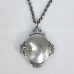 RARO RECIPIENTE PARA SANTO VIÁTICO  EM PRATA DE LEI COM INTERIOR EM RESPLANDECENTE  VERMEIL  APRESENTANDO-SE COMO SE DE OURO FORA . TAMBEM NO INTERIOR UMA LUNA BASCULANTE PARA ENCAIXAR A SANTA HÓSTIA. DE FEITIO OVAL APRESENTA DECORAÇAO COM ROCAILLES FENESTRADAS E CINZELADAS COM FEITIO DE PALMÁCEAS. PENDE DE UMA ESPESSO E LONGO COLAR. BRASIL, SEC. XVIII. 10 X 8 CM (O RECIPENTE) 84 CM DE COMPRIMENTO (COLAR PARA A PROCISSÃO) PESA 240 G NOTA: SANTO VIÁTICO é a Eucaristia recebida por aqueles que estão para deixar esta vida terrena e se preparam para a passagem à vida eterna. Recebida no momento da passagem deste mundo ao Pai, a Comunhão do Corpo e Sangue de Cristo morto e ressuscitado é semente de vida eterna e potência de ressurreição. A palavra viático vem do latim viaticum (de via, caminho), com o significado de provisão para o caminho. Este caminho é, para a Igreja, não só o caminho da terra, a vida corporal, mas também o caminho do céu, ou seja, a entrada, após a morte, na vida eterna. Para a Igreja, a Eucaristia, que é o mais importante dos sacramentos, sendo o mais excelente alimento espiritual da terra, é também a ajuda mais preciosa para o moribundo, quando está prestes a iniciar a "derradeira viagem". Segundo a fé católica, esta comunhão reveste um significado especial, porque "é semente de vida eterna e força de ressurreição", assim como "sacramento da passagem da morte para a vida, deste mundo para o Pai. A prática de levar a Eucaristia aos que se encontram prestes a morrer é um costume cristão atestado desde a antiguidade. Foi, aliás, a necessidade de conservar o pão consagrado fora da missa para estes casos que deu origem à Reserva eucarística, prática que se mantém ainda hoje pelo uso dos sacrários. O viático é, assim, o último sacramento do cristão, o verdadeiro sacramento da morte cristã. Na verdade, enquanto a Unção dos enfermos é dada a qualquer pessoa gravemente doente, ou em perigo de vida, mas que pode não estar propriamente à beira da morte, o viático é dado a quem efetivamente está prestes a morrer. A Eucaristia como viático, com a Penitência e a Unção dos enfermos, "constituem, quando a vida do cristão chega ao seu termo, os sacramentos que preparam a entrada na Pátria ou os sacramentos com que termina a peregrinação" A Eucaristia como viático é dada ao moribundo geralmente sob a forma do pão. No entanto, nos casos em que o moribundo não pode comungar desse modo, por dificuldades de deglutição, é permitido dar-lhe a comunhão somente com o vinho, que para esse efeito é conservado depois da missa (o que constitui excepção à regra habitual). Esta prática, aprovada pela Igreja, observa-se sempre que for necessário dar a comunhão a algum doente que não possa tomar o pão consagrado. Ao contrário da Unção dos enfermos, cuja administração está reservada, na Igreja Católica, aos presbíteros ou bispos, o viático pode também ser dado por um diácono e, em caso de necessidade, por um ministro extraordinário da comunhão. De São João Crisóstomo são estas palavras luminosas: "Por respeito a Divina Eucaristia, os Anjos fazem guarda de honra ao redor dos corpos dos escolhidos, que repousam no seio da terra."O Santo Viático, que Graça! Quando Santa Teresa de Ávila, já em perigo de morte, viu que ia se aproximando o Sacerdote com o Viático, para a surpresa de todos, pôs-se de rosto ardente e muito formoso, prosternando-se diante da Santa Hóstia, e exclama extática: "Senhor, já era tempo de nos vermos!" São Geraldo Majela pediu e recebeu o Santo Viático com uma piedade verdadeiramente angelical. E, quando a campainha anunciou a chegada da pequena procissão, São Geraldo se comoveu, e se transfigurou exclamando: "Eis que está vindo ao meu encontro o meu Senhor... Quanta dignação e delicadeza Ele tem para comigo!"O Santo Cura d'Ars, já moribundo, quando ouviu o som da campainha que anunciqava a chegada do Santo Viático, comoveu-se até as lágrimas, e disse: "Como conter as lágrimas quando Jesus vem a nós pela última vez com tanto amor?" Debret retratou uma procissão no Rio de Janeiro para levar o "São Viático" à casa de um moribundo. Naqueles tempos era costume corriqueiro tirar o chapéu e ajoelhar-se, ou mesmo acompanhar a procissão em que o Santo Viático passava, em direção à casa do enfermo (VIDE IMAGEM DA FIGURA DE DEBRET NOS CRÉDITOS EXTRAS DESSE LOTE)