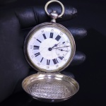 ROBERT GENEVE  GRANDE E RARO  RELOGIO DE BOLSO DO TIPO CAÇADOR  (TRES TAMPAS) COM DISPOSIÇÃO DO MOSTRADOR DITA MODELO  SAVONETTE (COROA NA POSIÇÃO DAS TRES HORAS O QUE OBRIGA O USUARIO A GIRAR O RELOGIO 45 GRAUS PARA CONSULTAR AS HORAS). CAIXA EM PRATA DE LEI. DIAL ESMALTADO EM BRANCO E AZUL. MECANISMO A CORDA COM CHAVE EXTERNA (CHAVE NÃO ACOMPANHA). EM MARCHA EMBORA FUNCIONE E PARE O QUE INDICA NECESSIDADE DE REVISÃO.  TAMPAS DIANTEIRA E TRASEIRA PROFUSAMENTE CINZELADAS. SUIÇA, FINAL DO SEC. XIX OU INICIO DO XX. 58 MM DE DIAMETRO